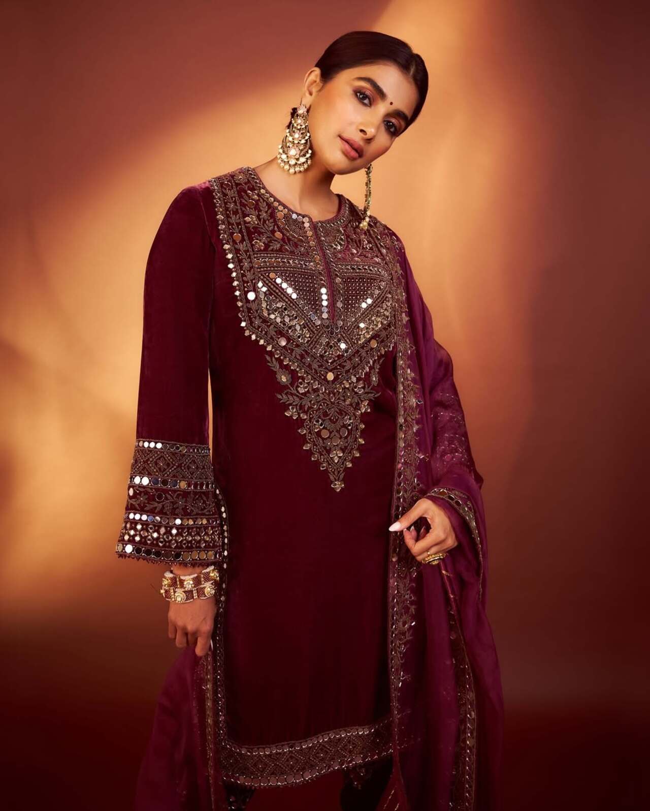 Draped in a rich maroon velvet ensemble, Pooja brings regal allure to festive fashion. The mirror and zari work on her kurta and dupatta exude luxury